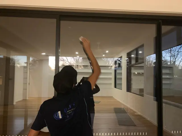A Blue Cleaning Group cleaner wiping a full-height glass sliding door in an empty house with timber floors